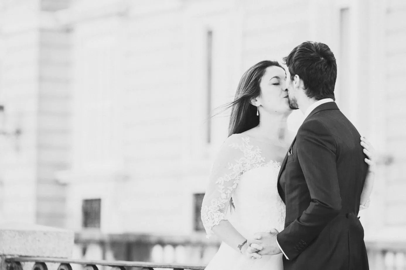 Pareja de boda besándose y tomados de las manos frente a un edificio.
