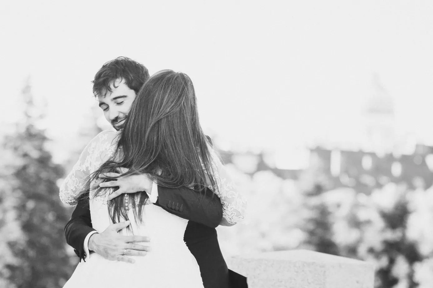 Pareja abrazándose al aire libre en blanco y negro, fondo urbano desenfocado.