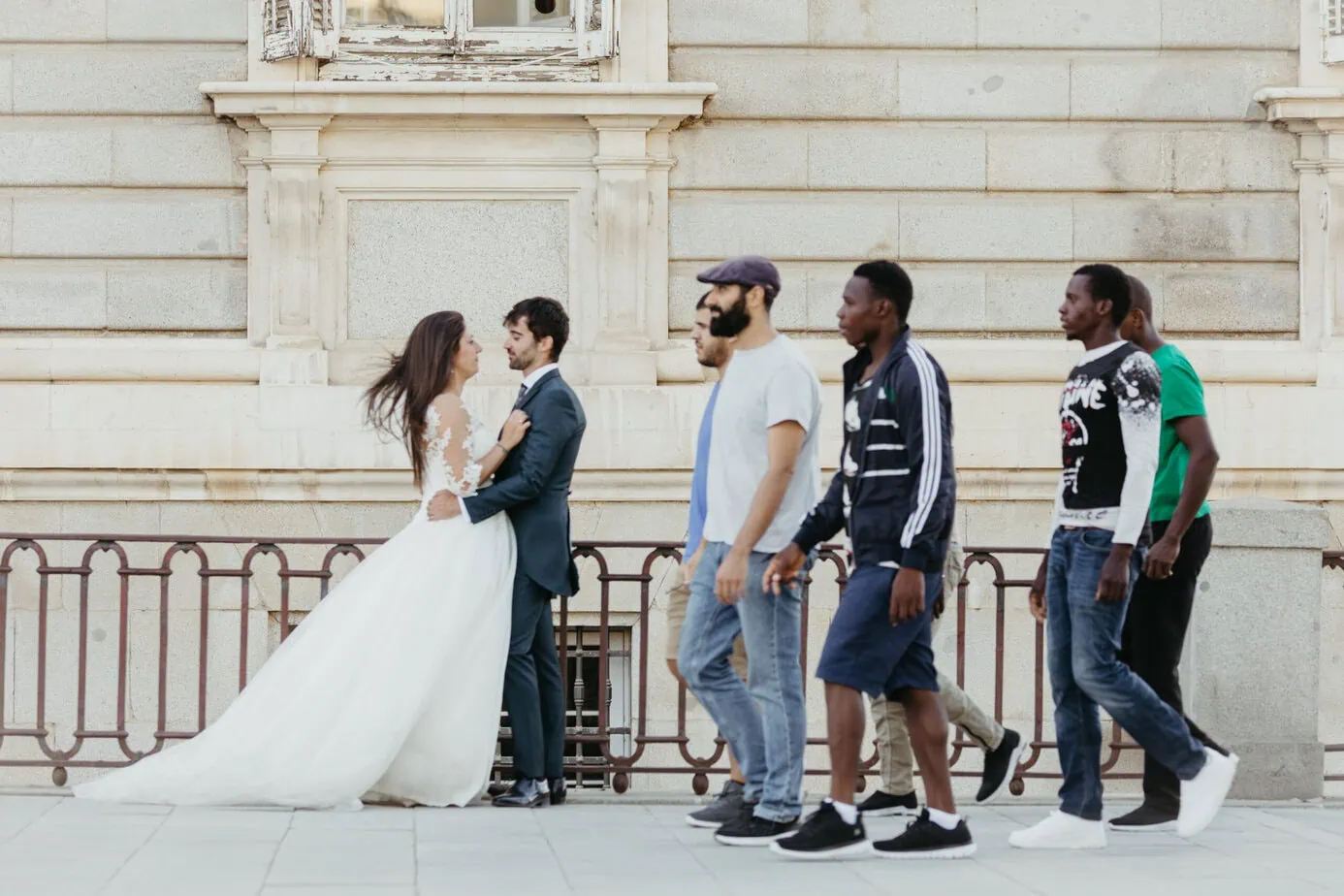 Pareja de boda frente a edificio con transeúntes caminando por la acera.