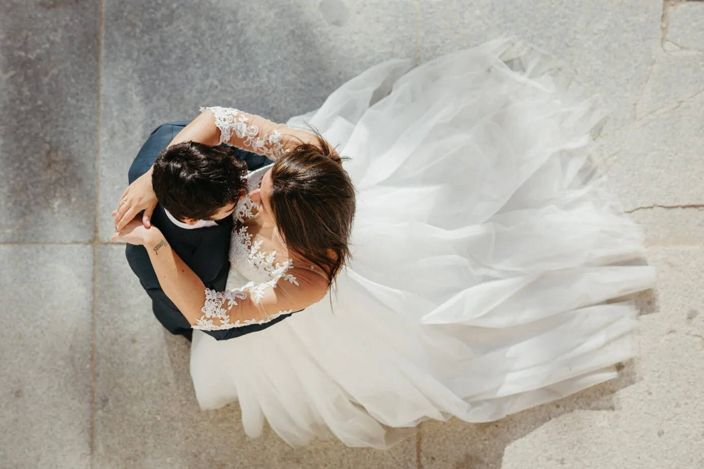 Vista aérea de pareja abrazada; mujer lleva vestido de novia blanco con encaje.