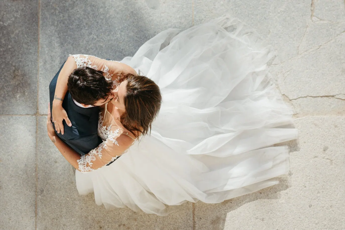 Pareja abrazándose, uno con traje oscuro y otro con vestido de novia blanco en suelo claro.