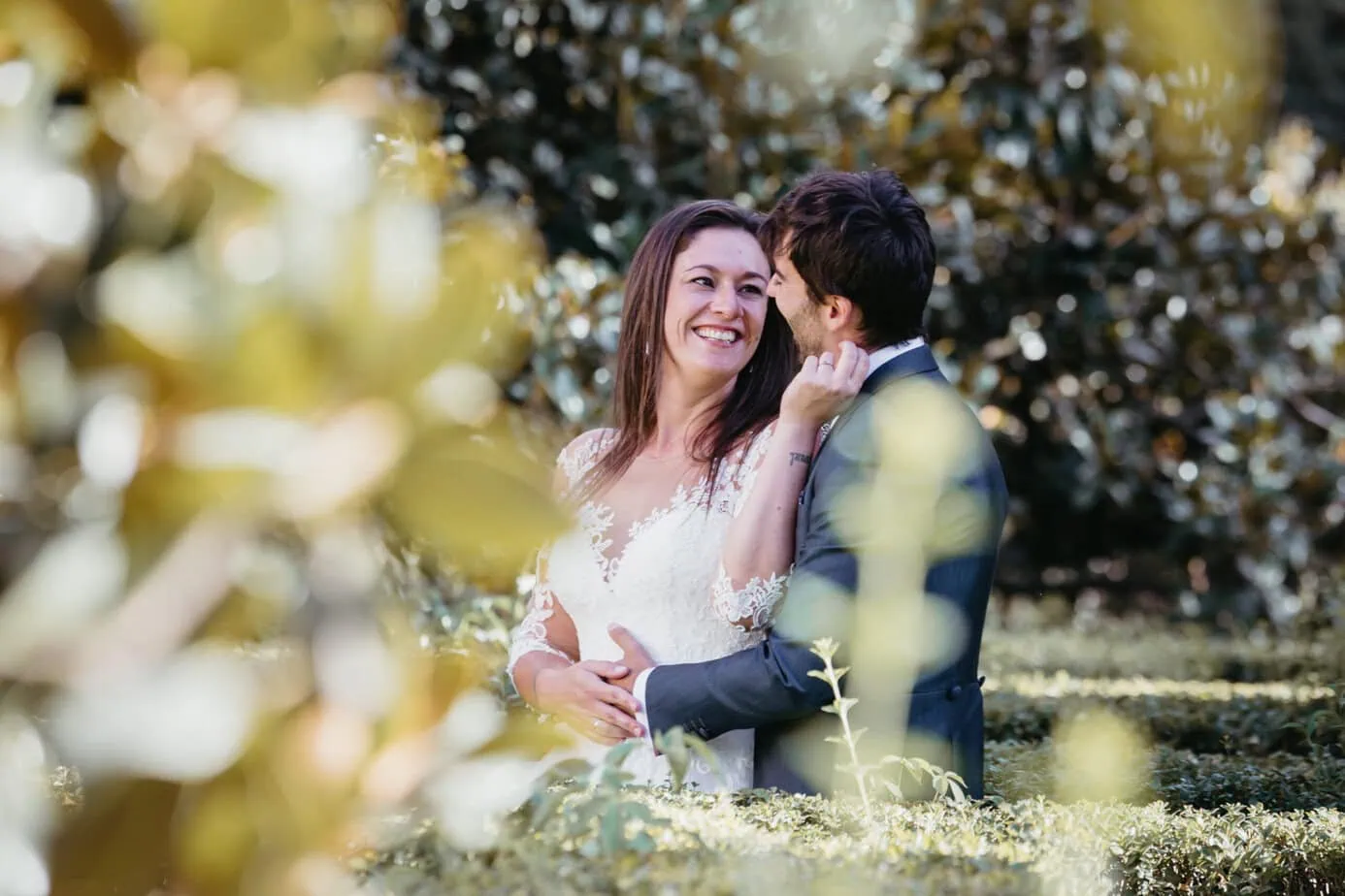 Pareja elegante abrazada en un paisaje al aire libre rodeado de vegetación.